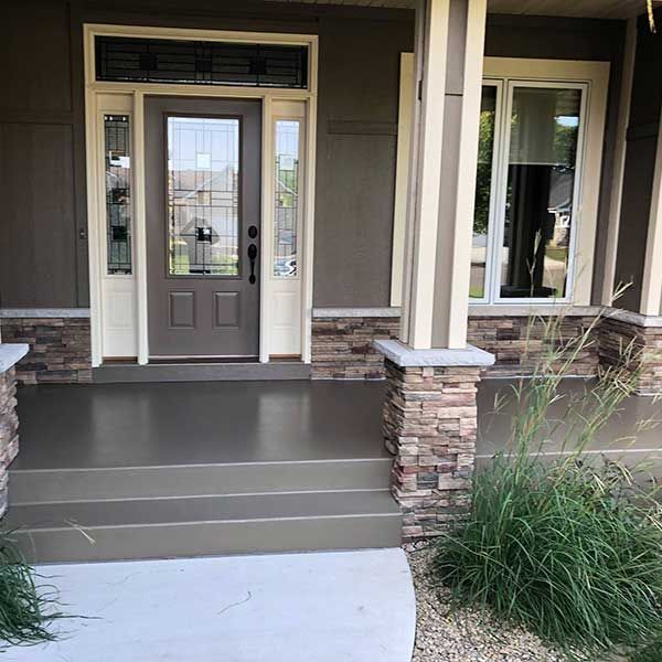 Front porch with gray steps, tan columns, and a brown front door at a house entrance