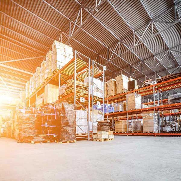 Bright warehouse interior with tall shelving, stacked boxes, and sunlight streaming in from the left.