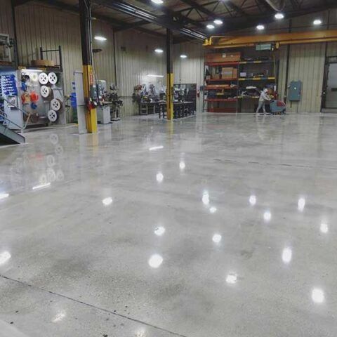 Spacious industrial workshop with a polished concrete floor, metal shelves, and overhead lights.