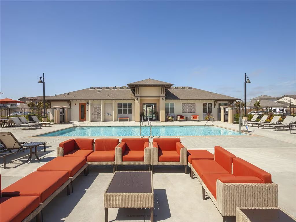 Modern resort pool with orange lounge seating and a central cabana under a clear blue sky