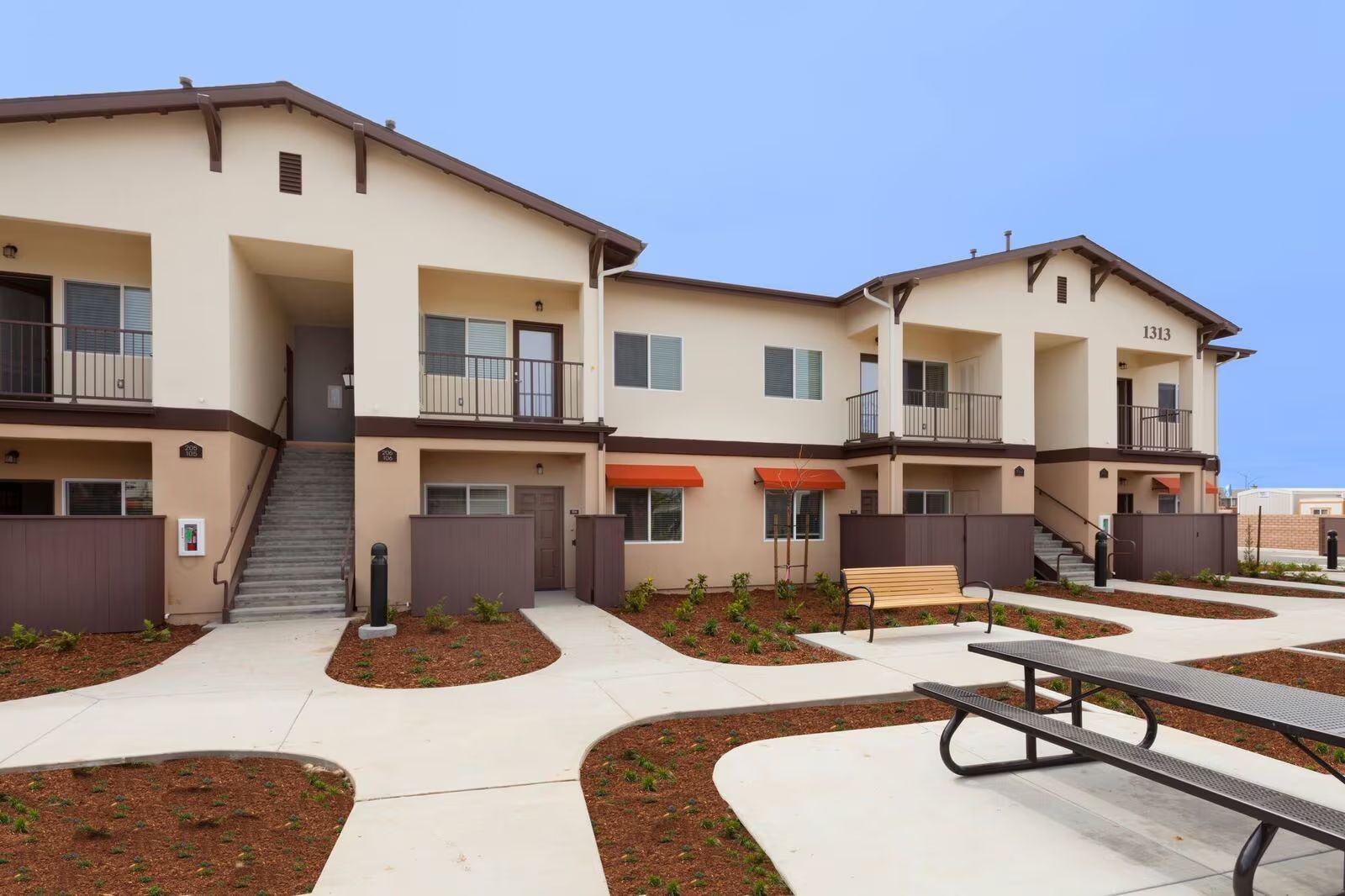 Apartment complex courtyard with tan buildings, staircases, balconies, and picnic tables