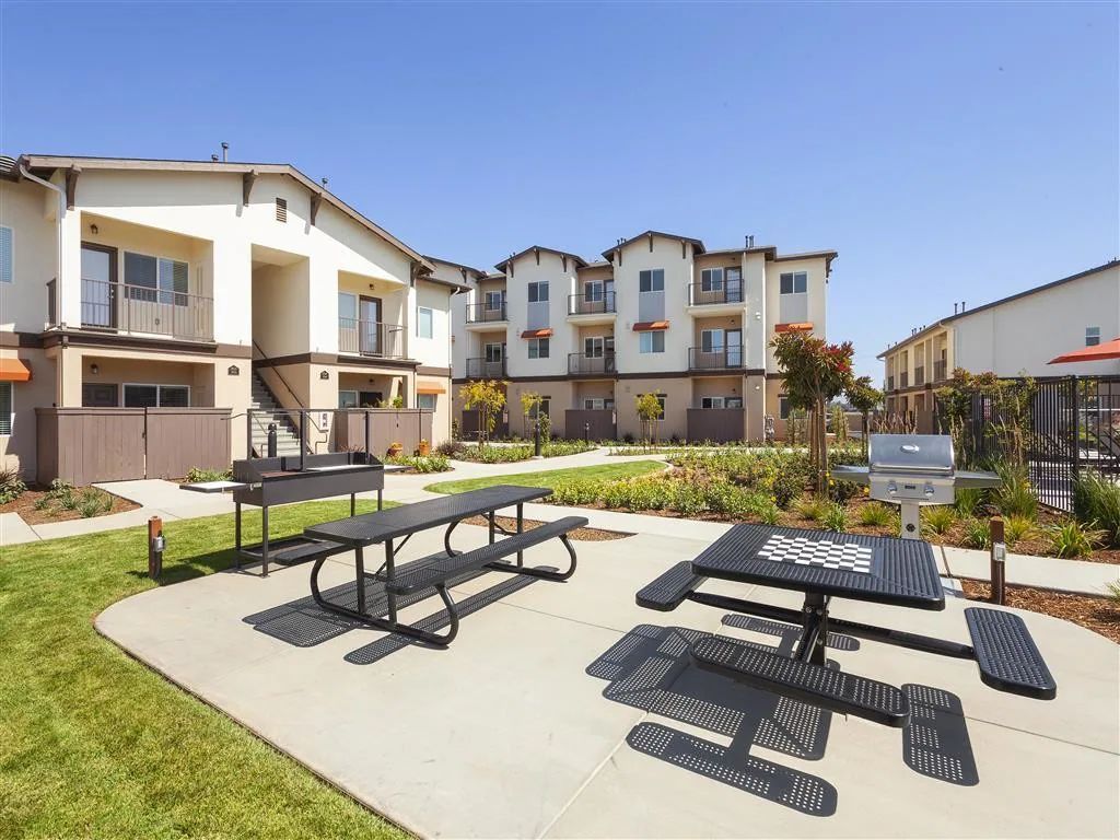 Courtyard with picnic tables and benches beside modern apartment buildings on a sunny day