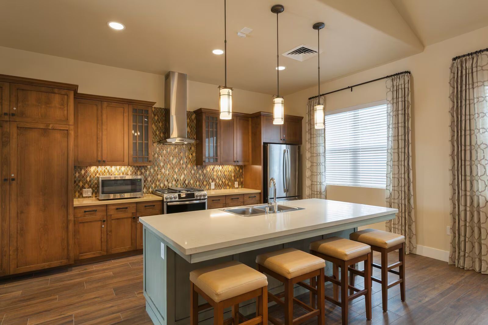 Modern kitchen with wood cabinets, white island, and three stools under pendant lights