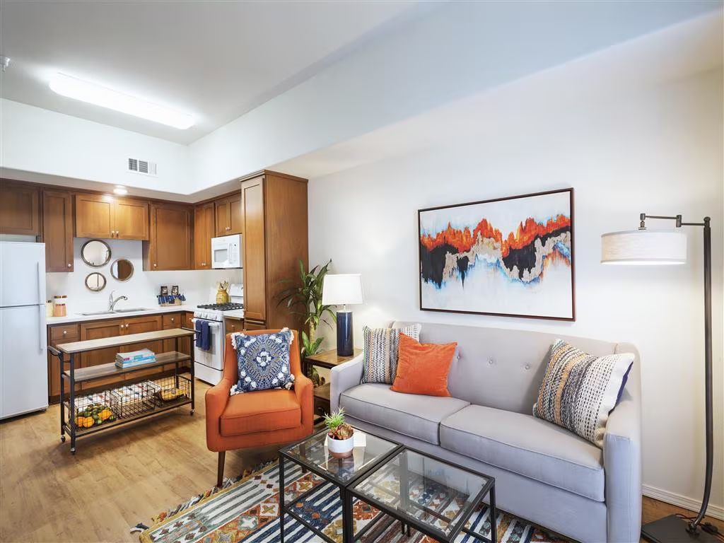 Open-concept living room and kitchen with gray sofa, orange chair, and glass coffee table