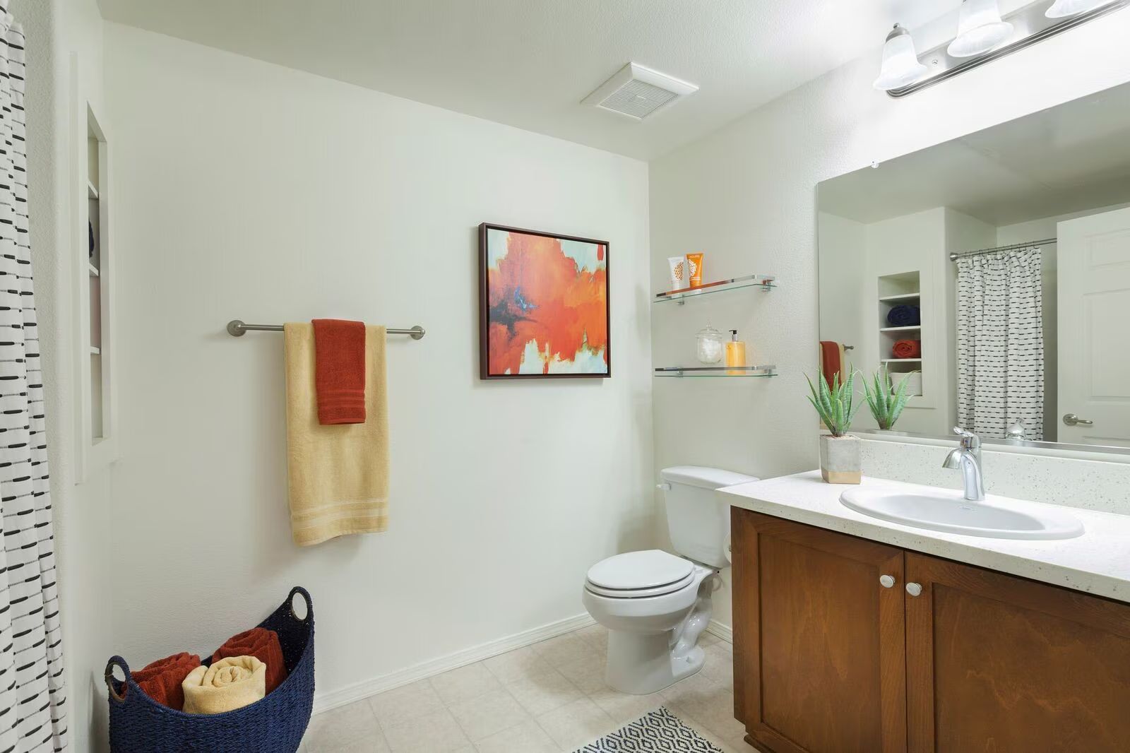 Bright bathroom with white walls, wood vanity, wall art, towel, toilet, and a small basket near the sink.
