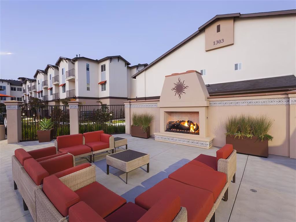 Outdoor patio with red sectional seating, fire pit, and apartment buildings at dusk