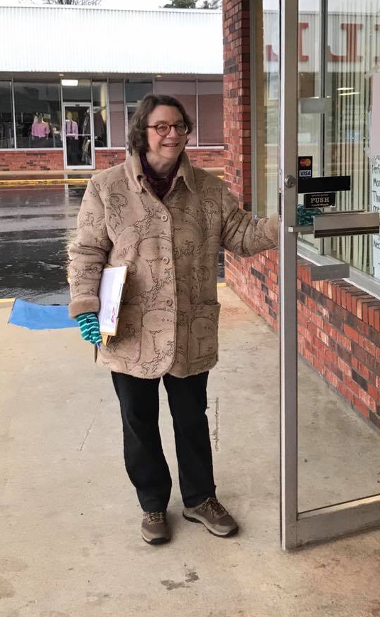 A woman in a coat is standing in front of a glass door.