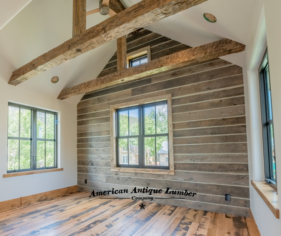 Horizontal grey siding with chink joint on accent interior wall with windows and reclaimed hand hewn trusses. 