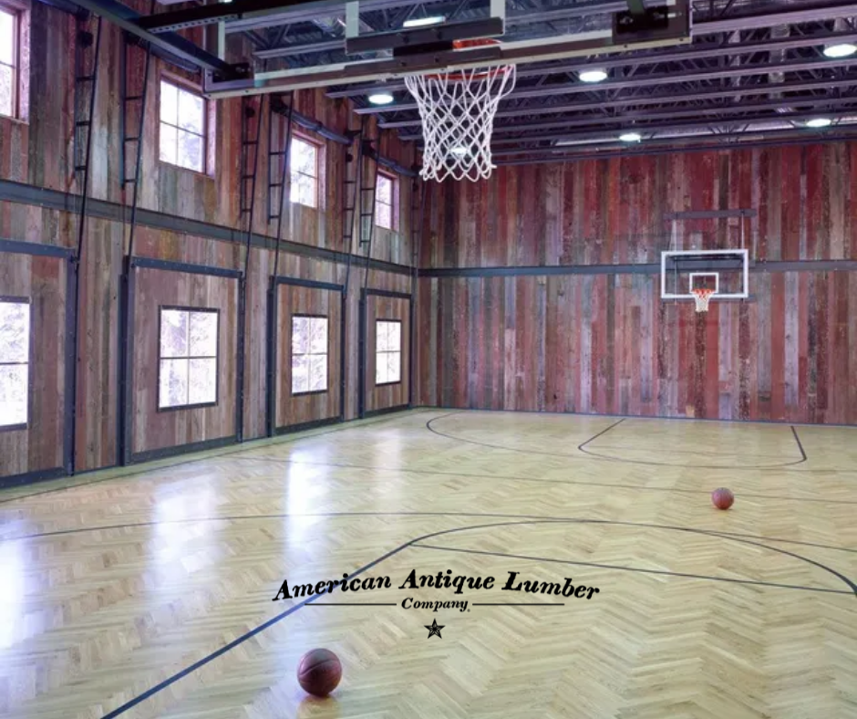 Light blonde herringbone basketball court floor with bank of windows on the left and reclaimed faded red face barn wood siding as wall cladding. 