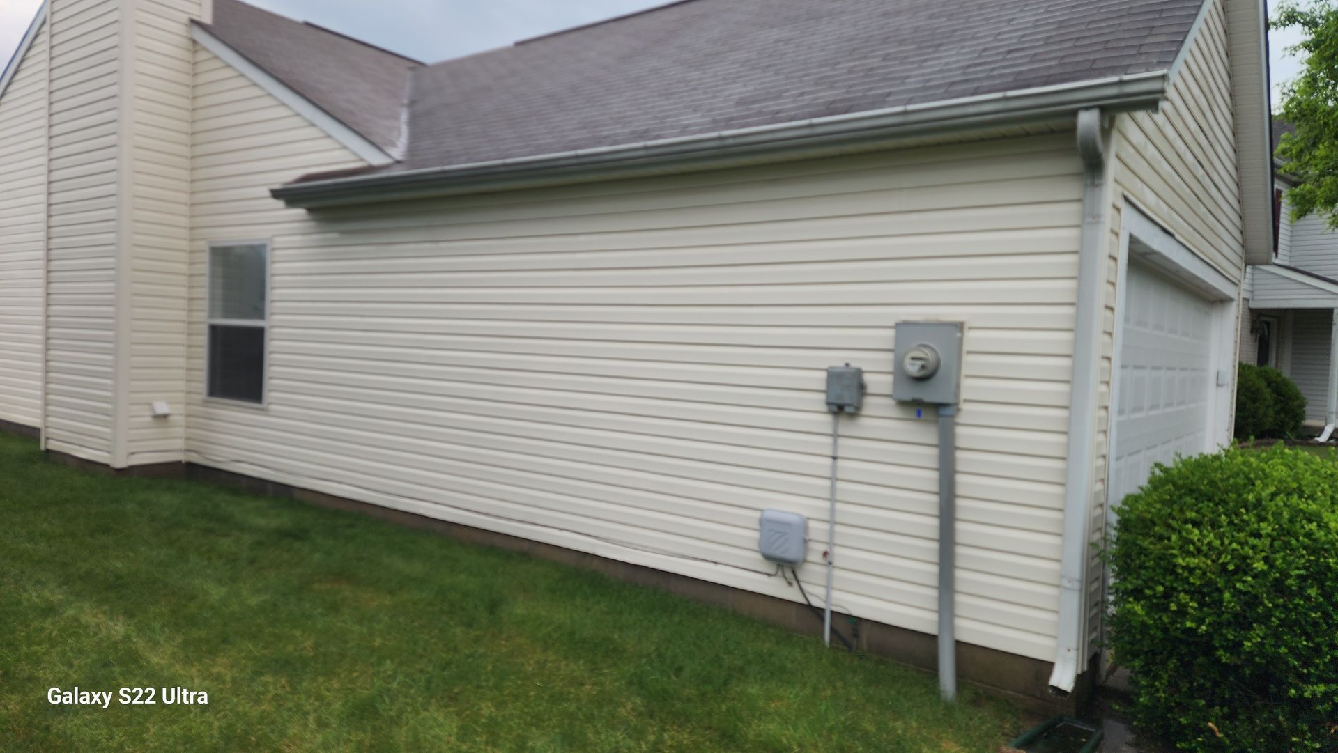 Side view of a beige house with gray siding, lawn, utility meters, and a white garage door.
