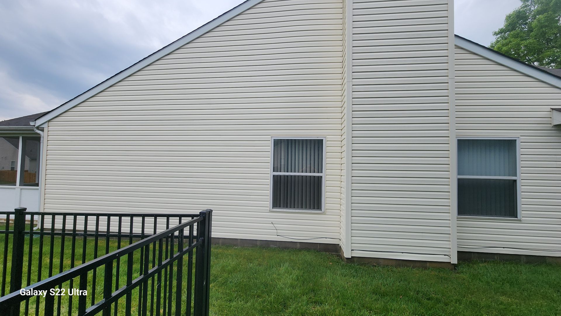 White house with horizontal siding and fenced green lawn under a cloudy sky.