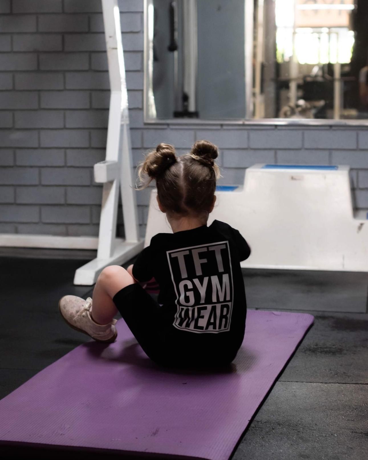 A Little Girl Wearing a TFT Gym Wear Shirt Sits on a Yoga Mat — The Factory Gym in Taree, NSW