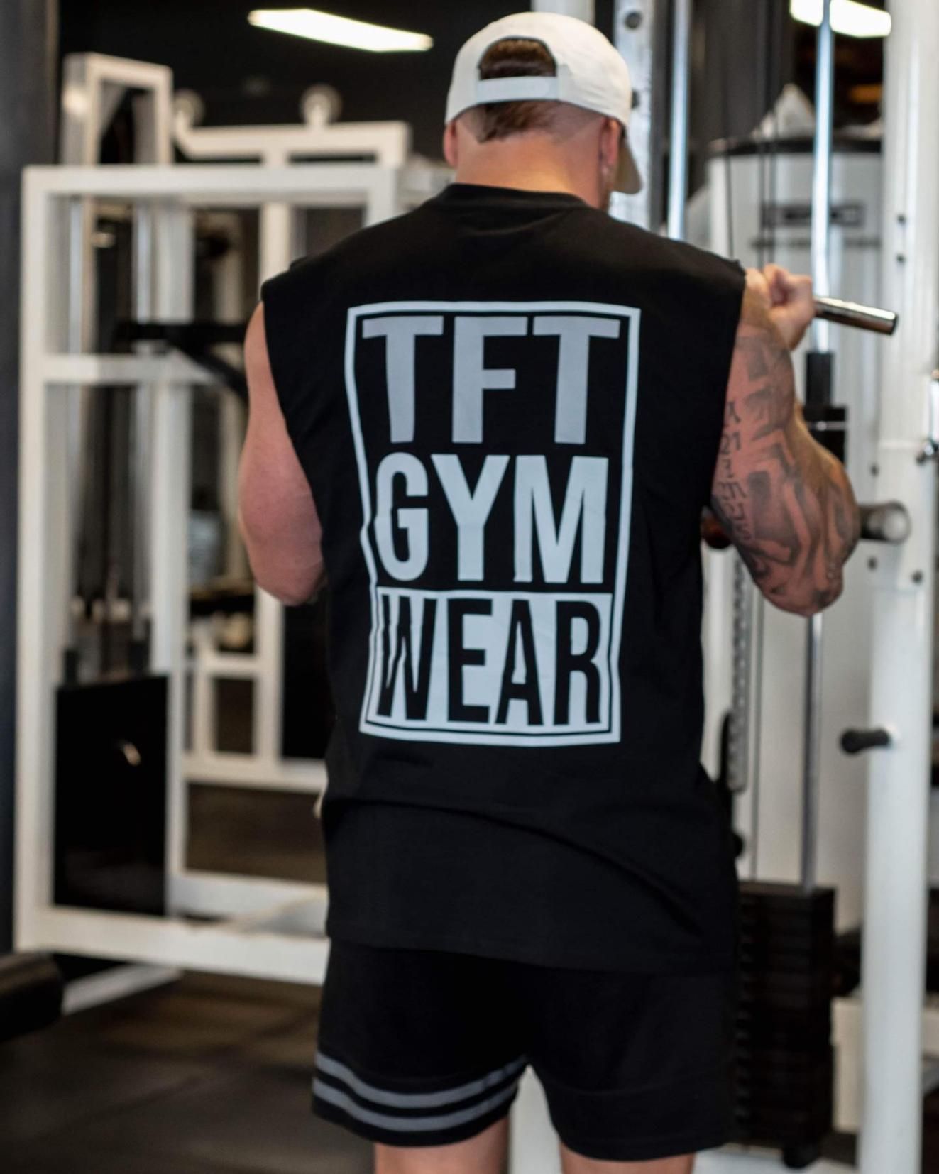 A Man is Squatting on a Machine in a Gym Wearing a TFT Gym Wear Tank Top — The Factory Gym in Taree, NSW