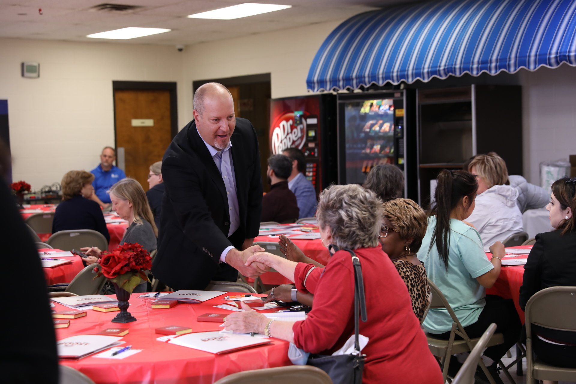 A man in a suit shakes hands with a woman at a table