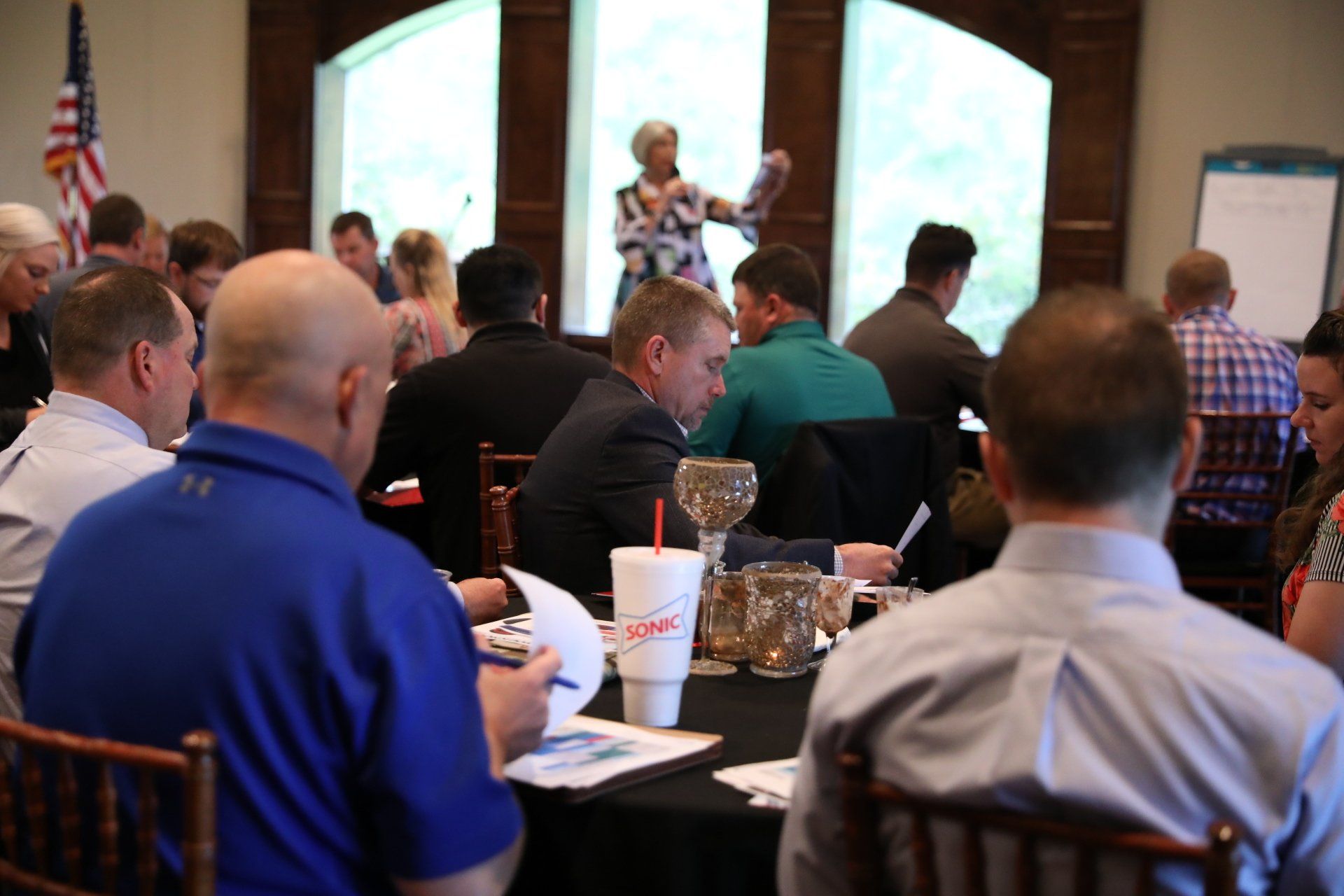 A woman is giving a presentation to a group of people sitting at tables.