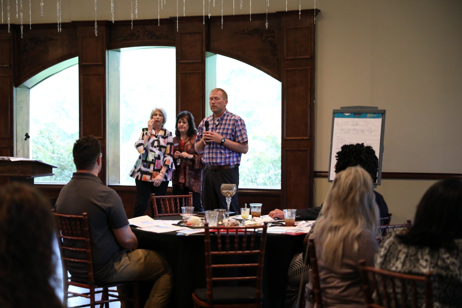 A man is giving a presentation to a group of people sitting at tables.