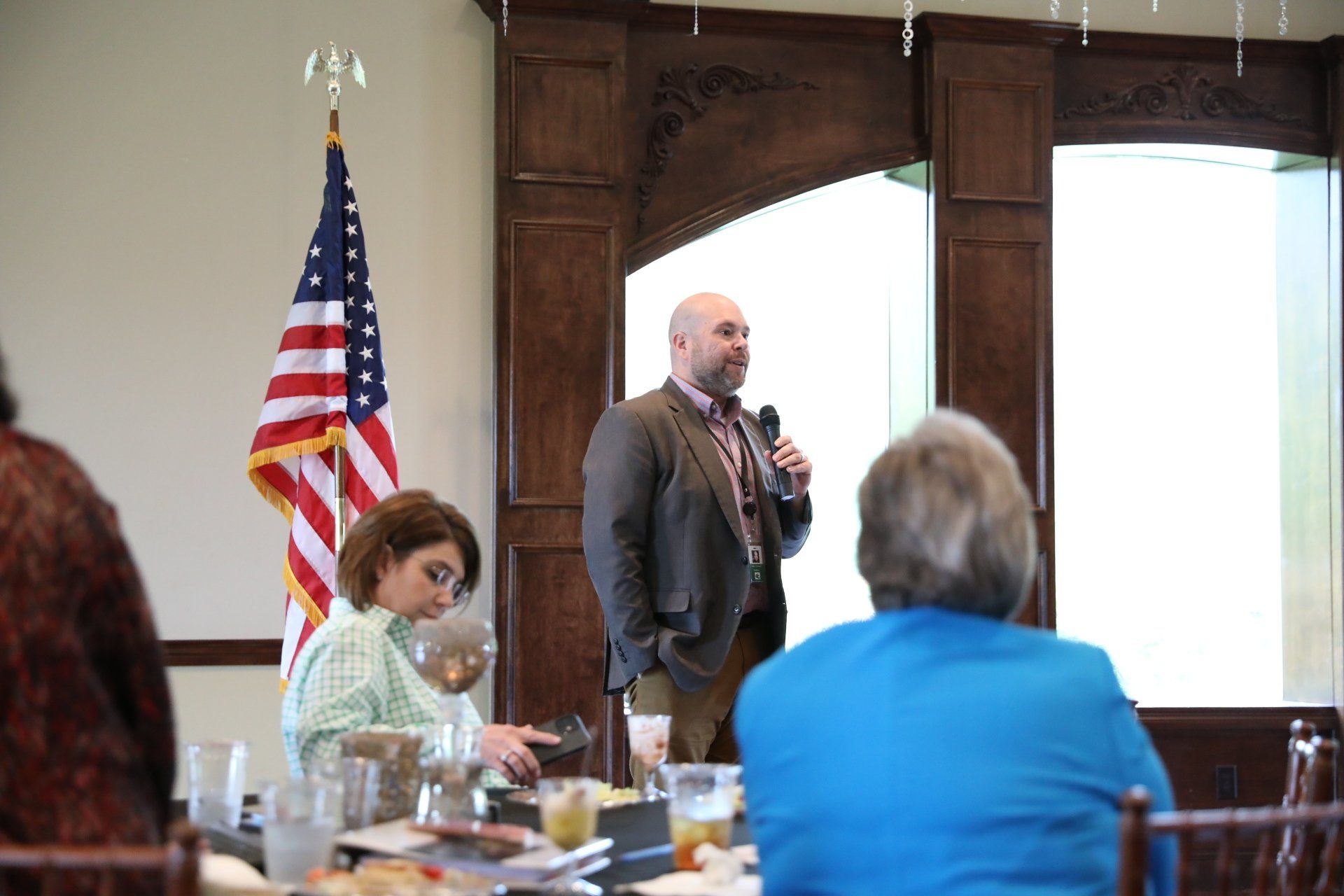 A man is holding a microphone in front of a group of people sitting at a table.