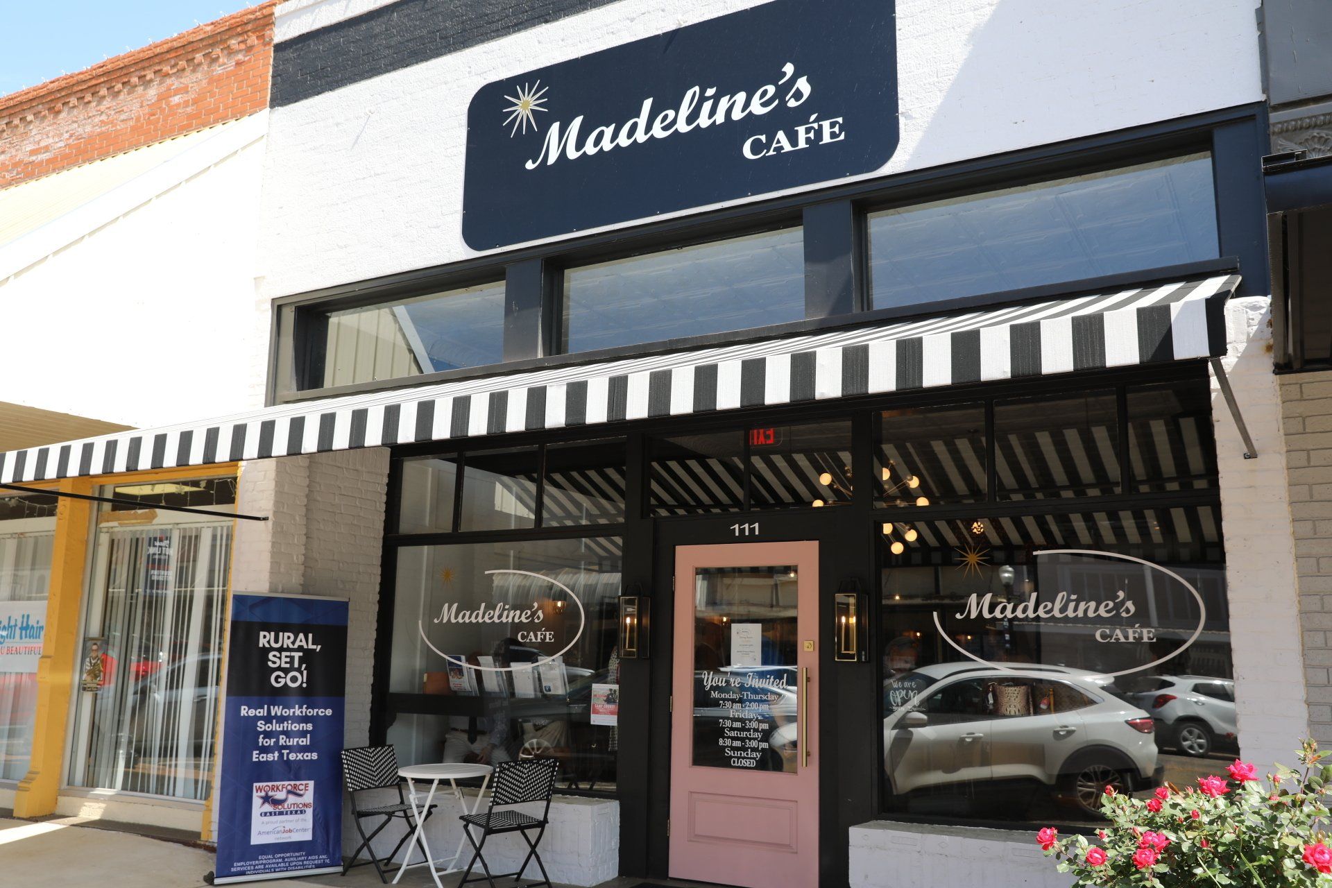 The front of madeleine 's cafe with a black and white awning.