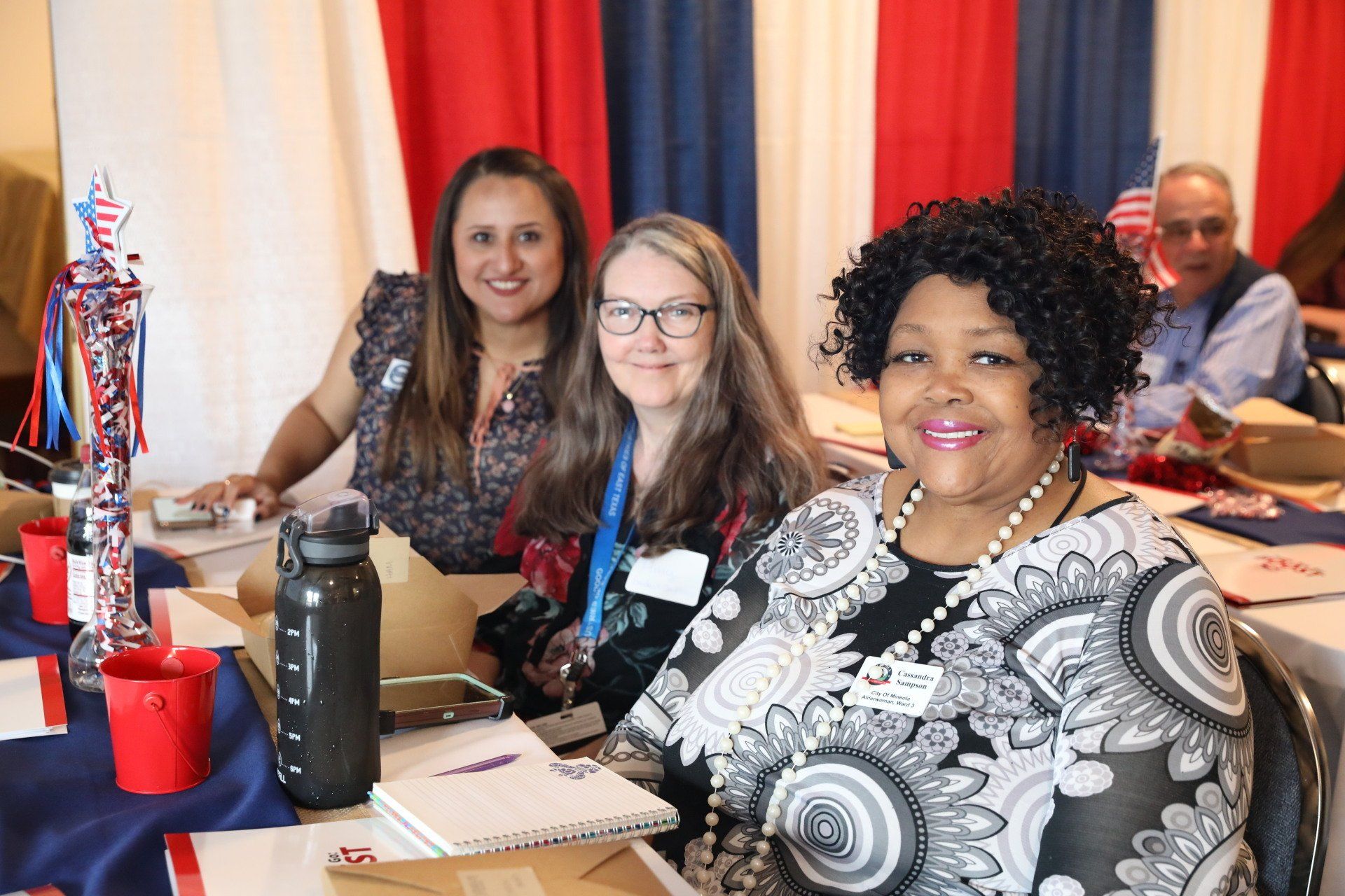 Three women are sitting at a table with a water bottle.