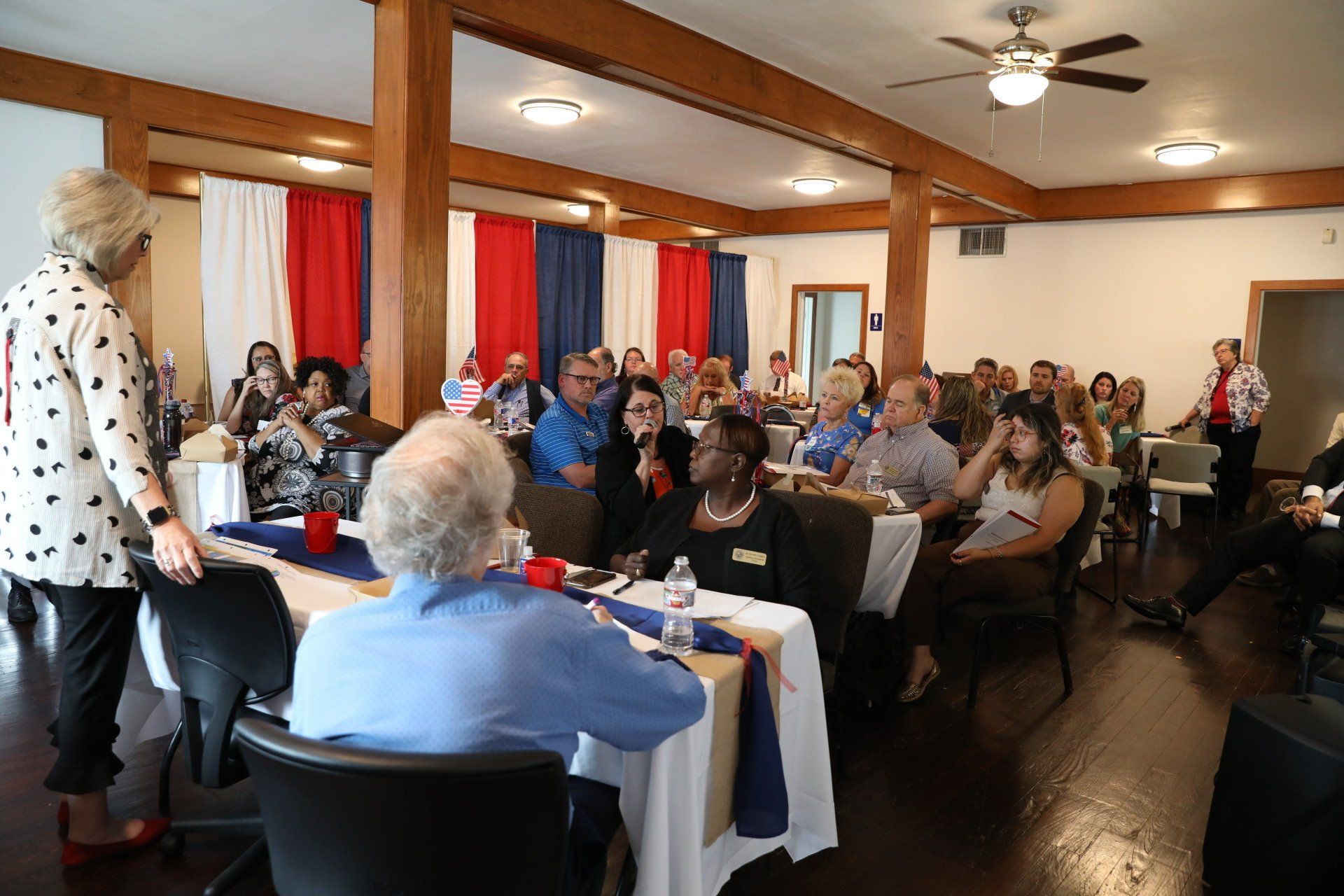 A woman is giving a presentation to a group of people sitting at tables in a room.