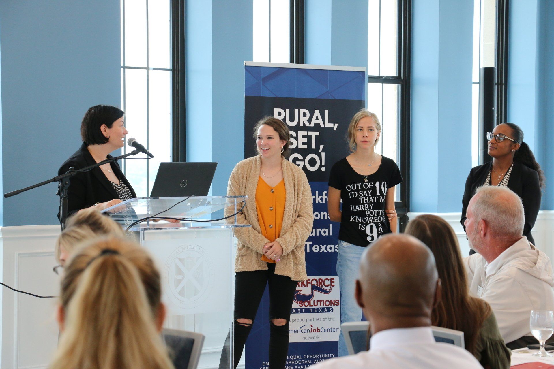 A woman is standing at a podium giving a presentation to a group of people.