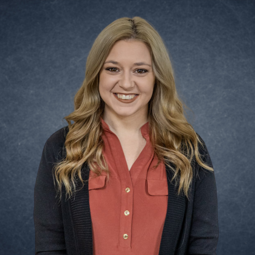 Smiling woman in a red blouse and dark cardigan against a blue studio background