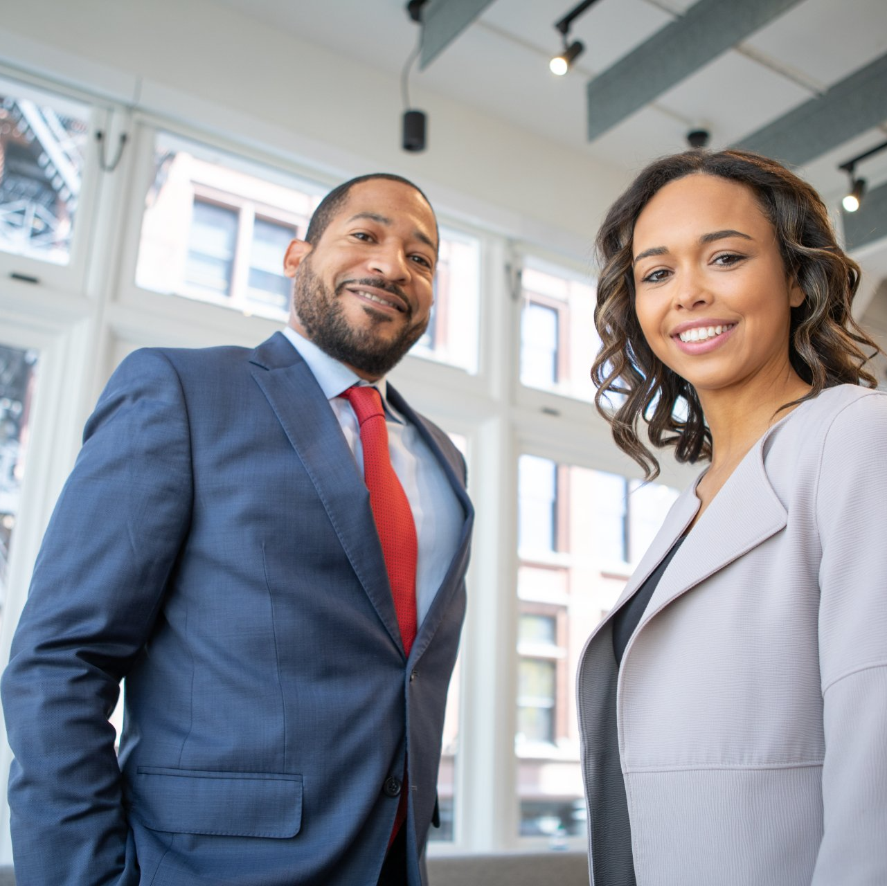 A man in a suit and tie stands next to a woman in a grey jacket