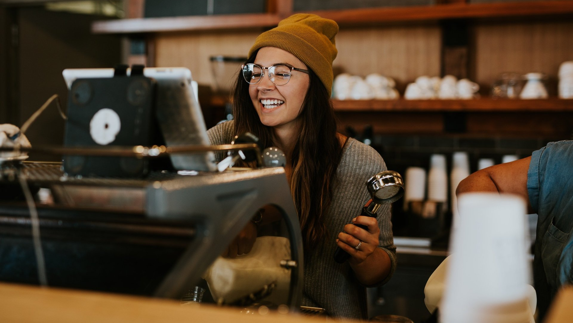 A woman is sitting at a counter in a coffee shop holding a cup of coffee.