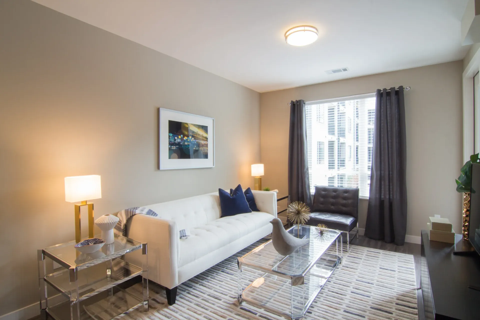 Modern apartment living room with a white sofa, glass coffee table, and dark curtains at Chroma, offers apartments near UMSL.