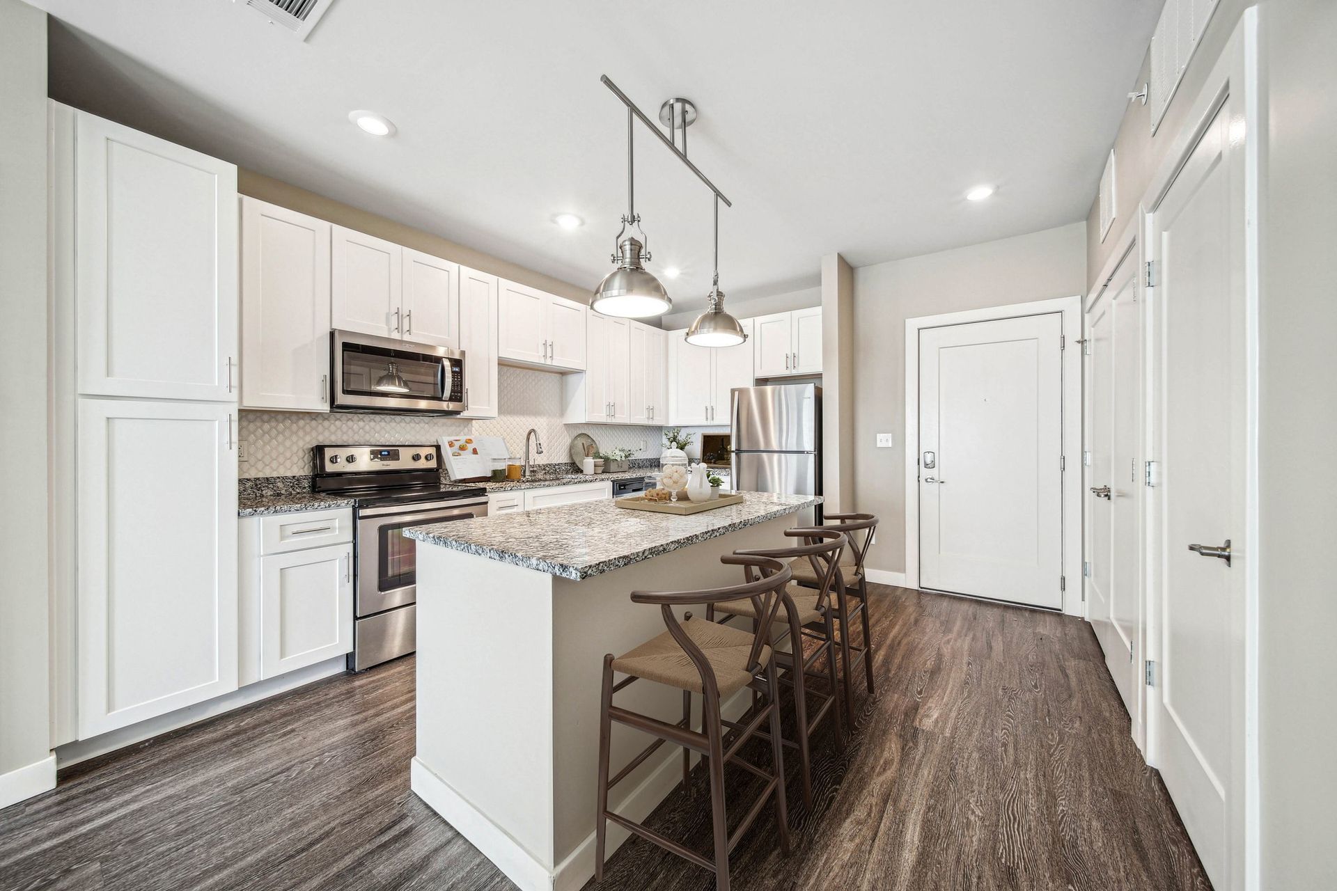 Modern white kitchen with granite countertops, island seating, and stainless steel appliances at Chroma, offers apartments in St. Louis MO.