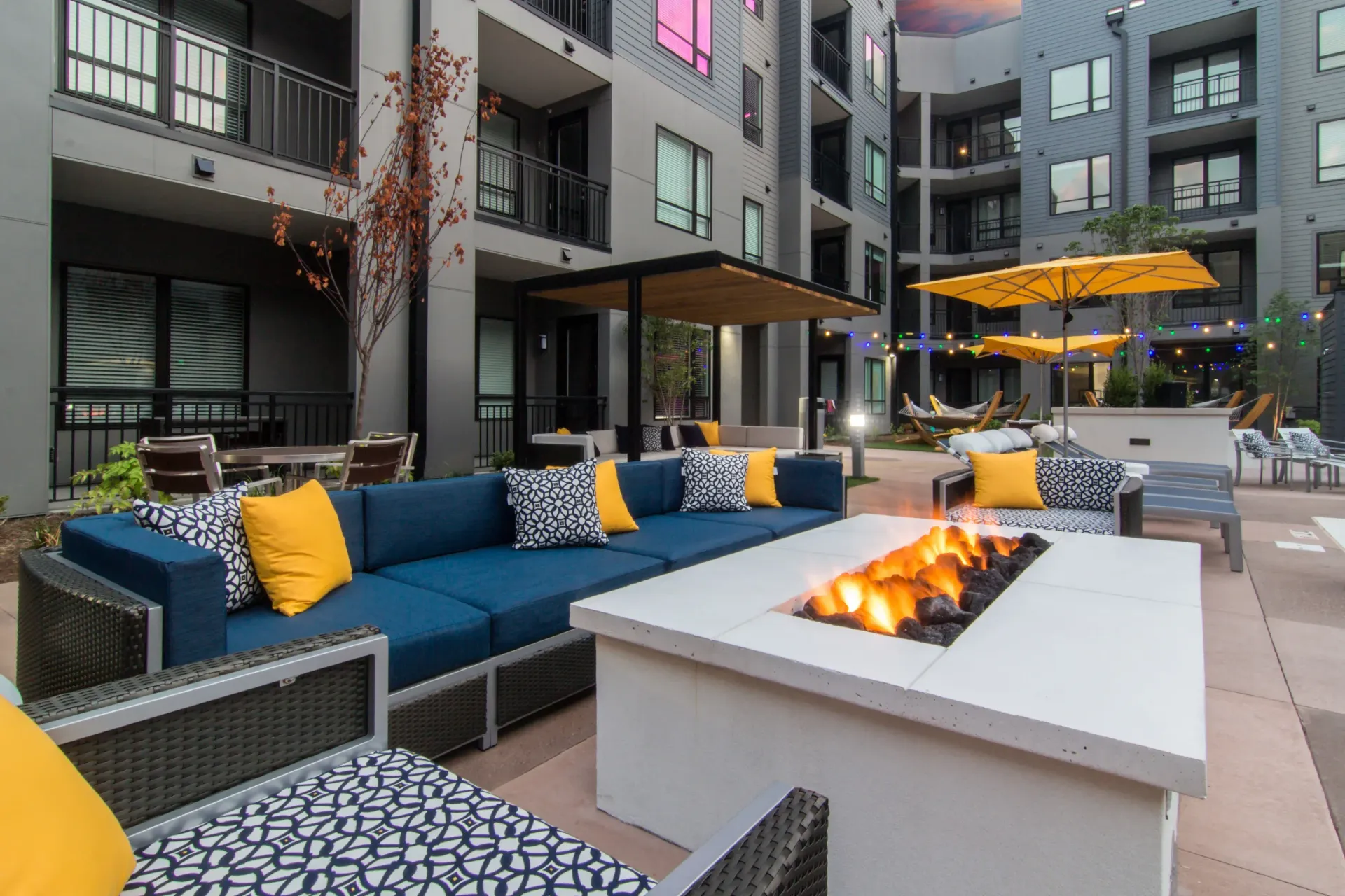 Outdoor community courtyard with a gas fire pit, blue sectional seating, and yellow accent cushions at Chroma, offers apartment complex in St, Louis, MO.