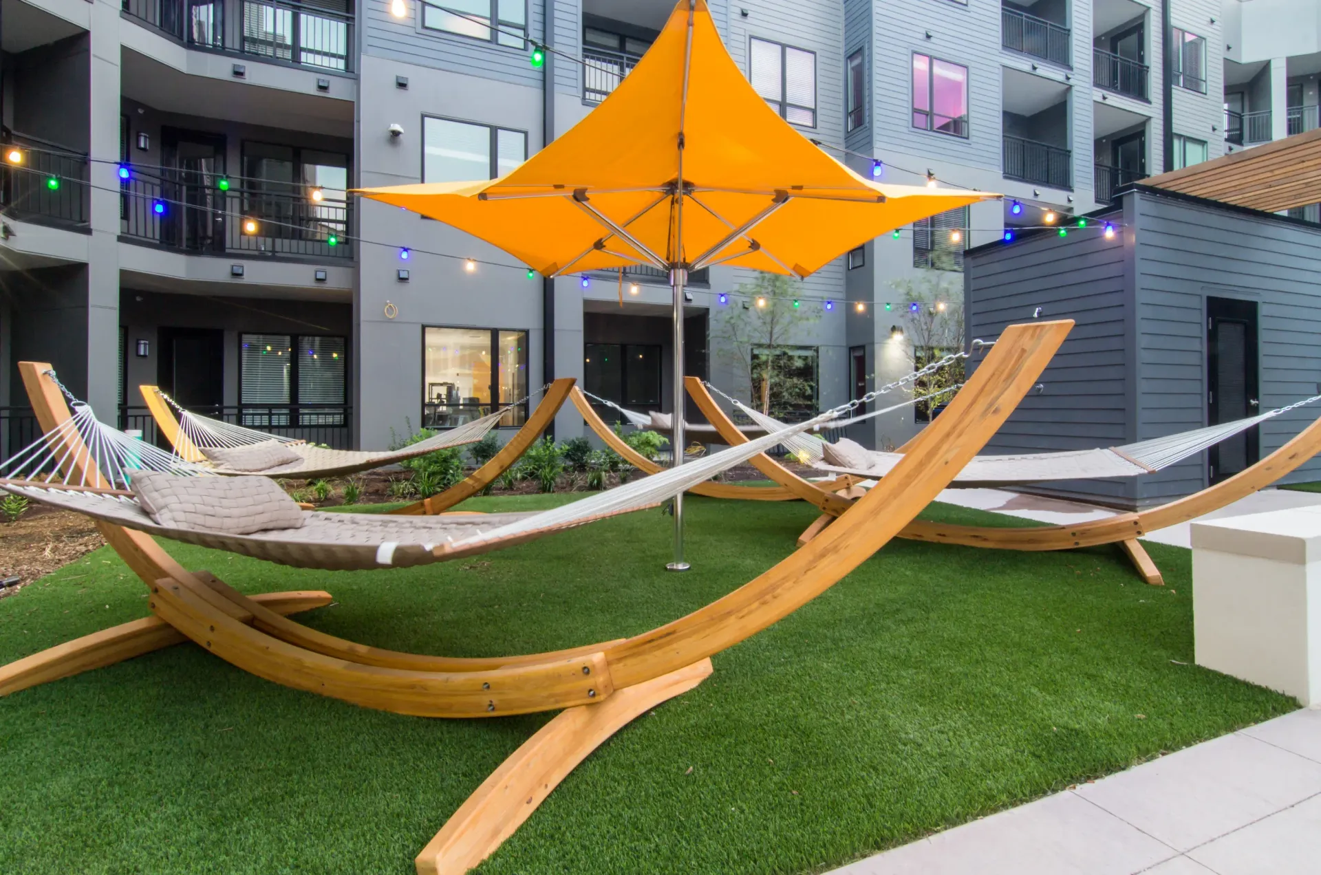 Outdoor community courtyard with curved wooden hammocks and string lights under an orange canopy at Chroma, offers apartments to rent in St Louis.