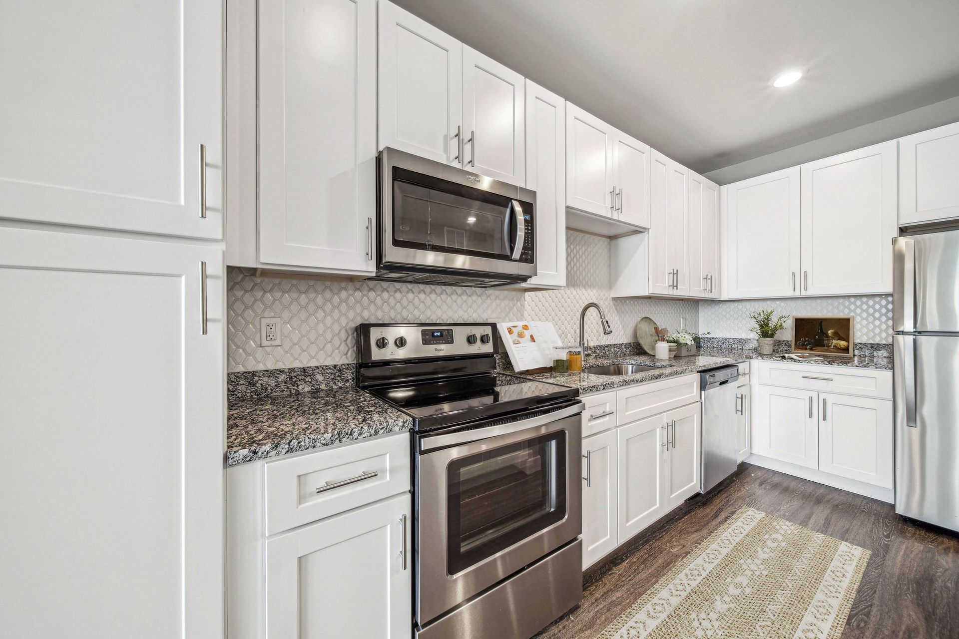 Modern white kitchen with granite countertops, stainless steel appliances, and a double sink at Chroma, offers The Grove apartments for rent in St Louis.