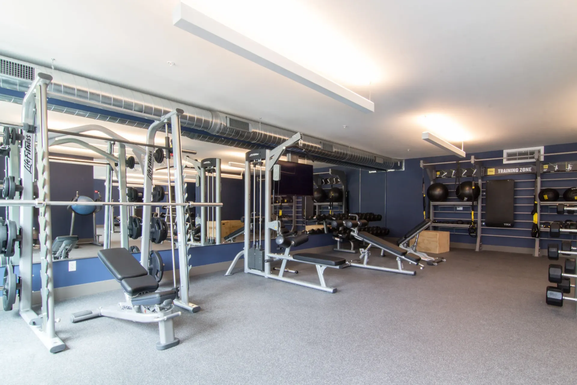 Indoor fitness center with weight machines, benches, and dumbbell racks at Chroma, offers apartments in The Grove.