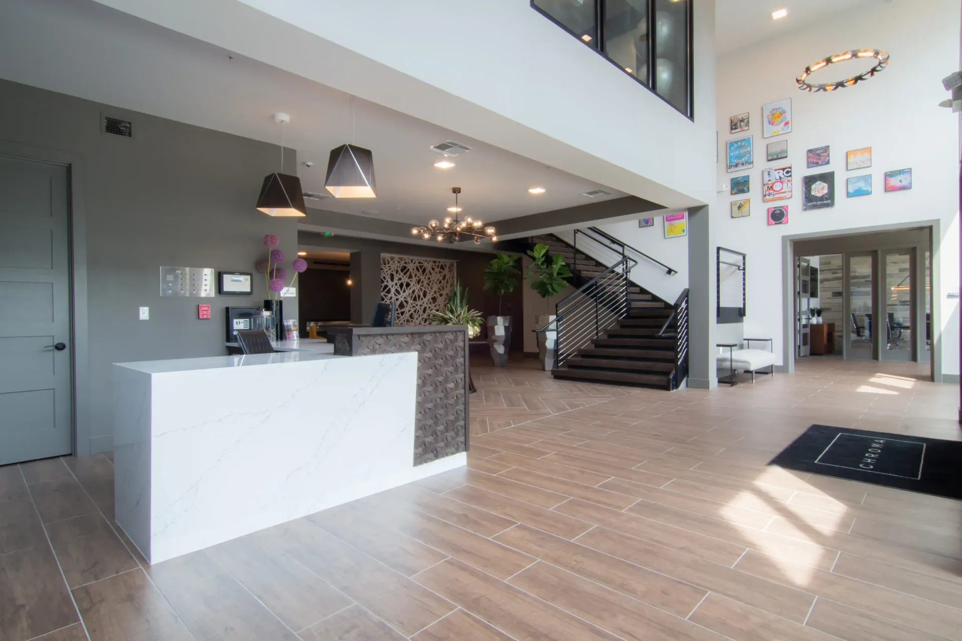 Modern apartment lobby with a white marble-front reception desk, staircase, and wall art at Chroma, offers St Louis MO luxury apartments.