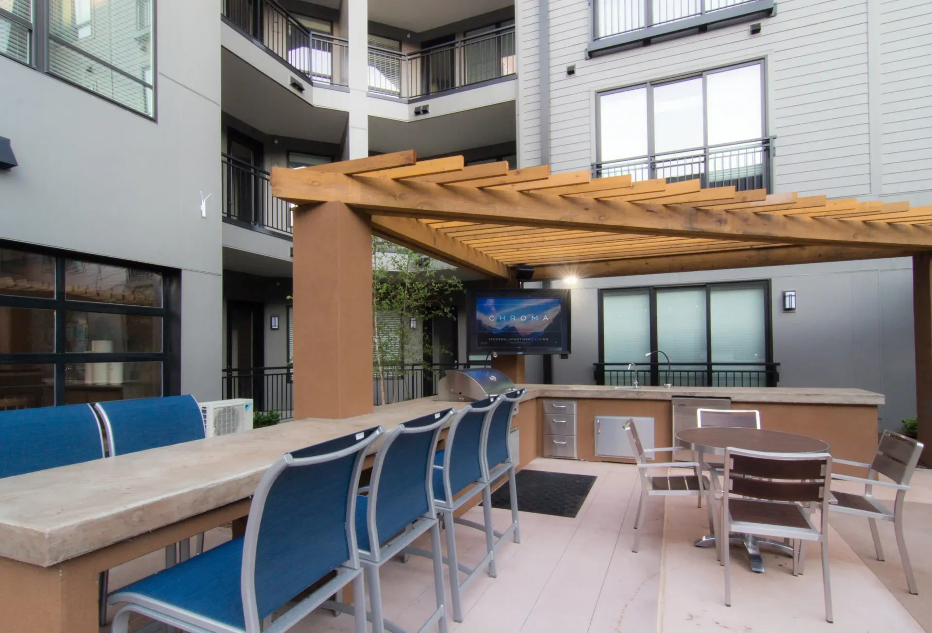 Outdoor community grilling area with seating under a wooden pergola at an apartment complex at Chroma, offers apartments in STL.