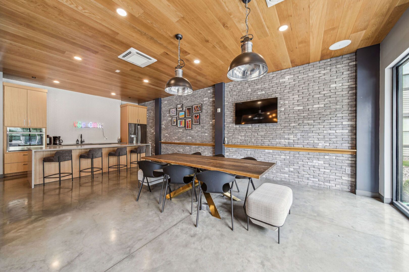 Communal lounge with brick accent wall, long wooden table, bar seating, and a wall-mounted TV at Chroma, offers apartments for rent St Louis South City.