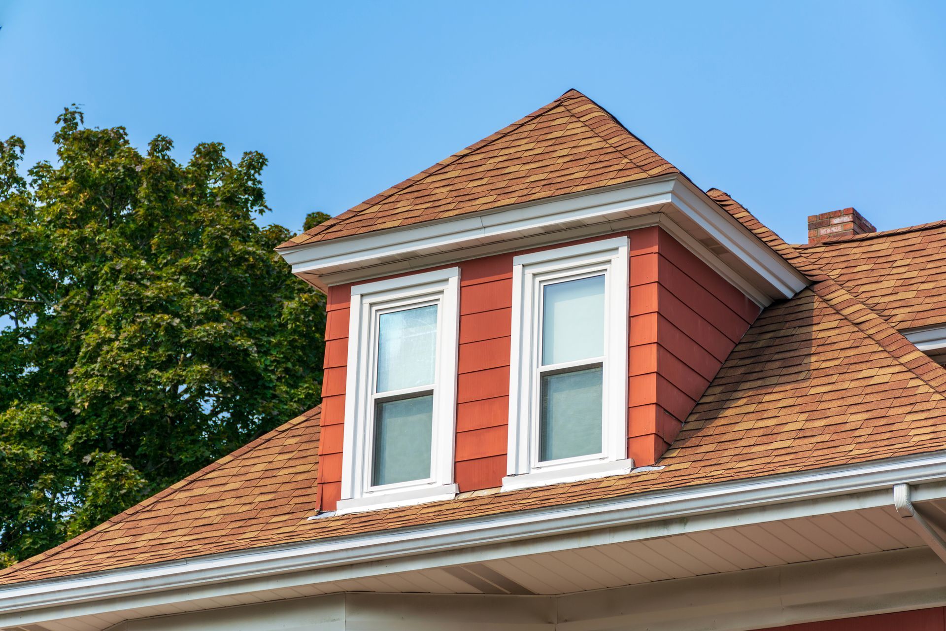 Dormer window with white trim on a red-brick house roof under a blue sky Dormer window with white trim on a red-brick house roof under a blue sky