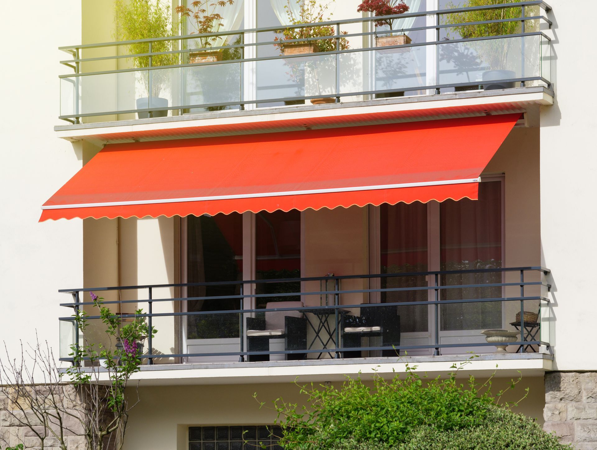 Balcony with a bright red awning, glass doors, and potted plants on an apartment facade Balcony with a bright red awning, glass doors, and potted plants on an apartment facade