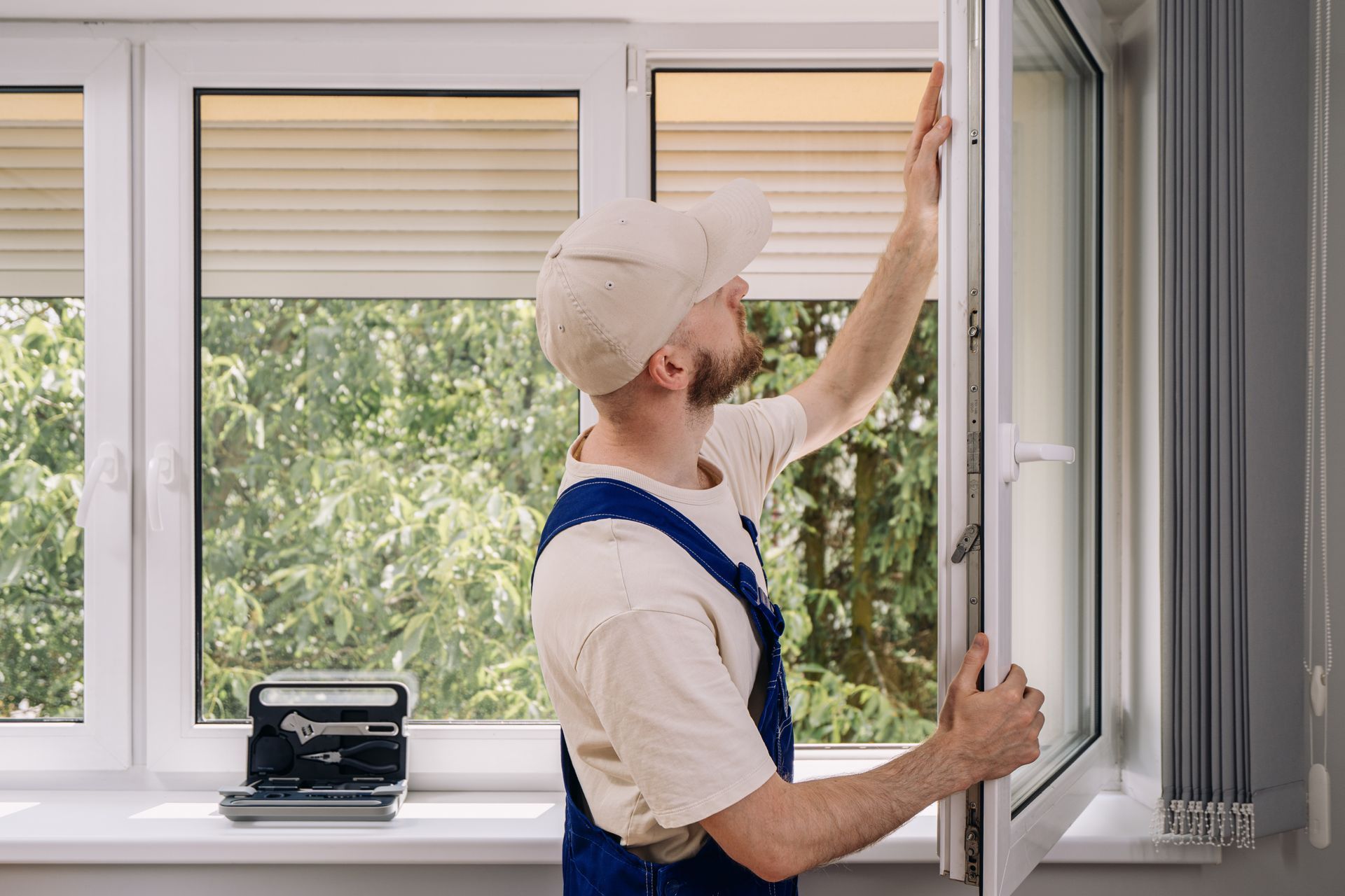 Technician adjusting a window blind in a bright room with a toolbox on the sill