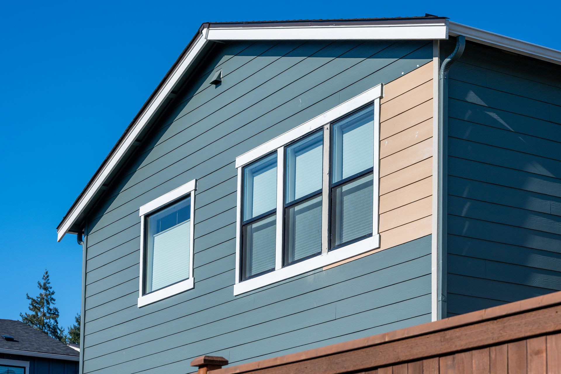 Blue house exterior with gray siding, white-trimmed windows, and a brown fence under a clear sky Blue house exterior with gray siding, white-trimmed windows, and a brown fence under a clear sky