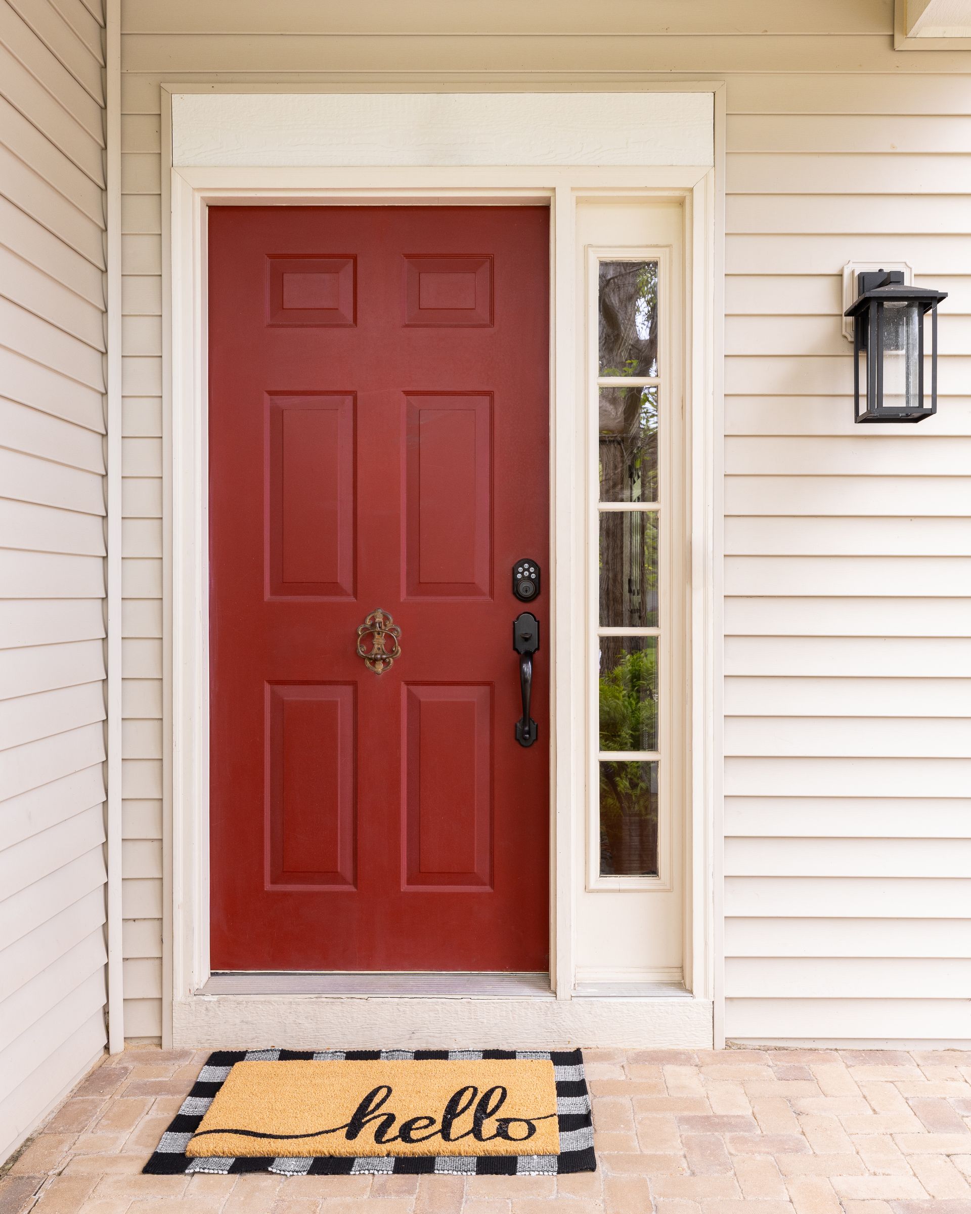 Red front door with a hello doormat and black wall lantern beside it Red front door with a hello doormat and black wall lantern beside it