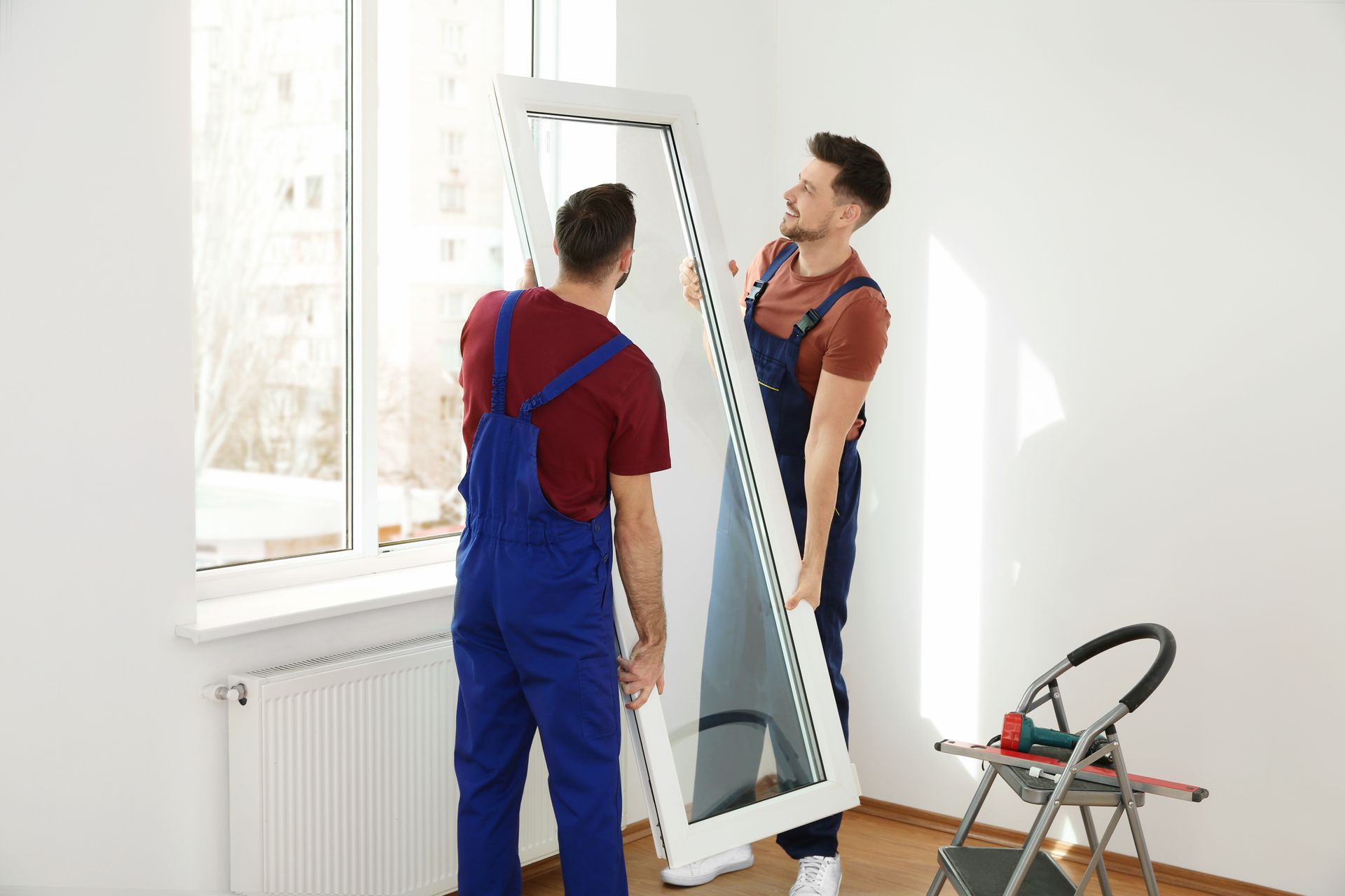 Two workers moving a tall mirror near a window in a bright room Two workers moving a tall mirror near a window in a bright room