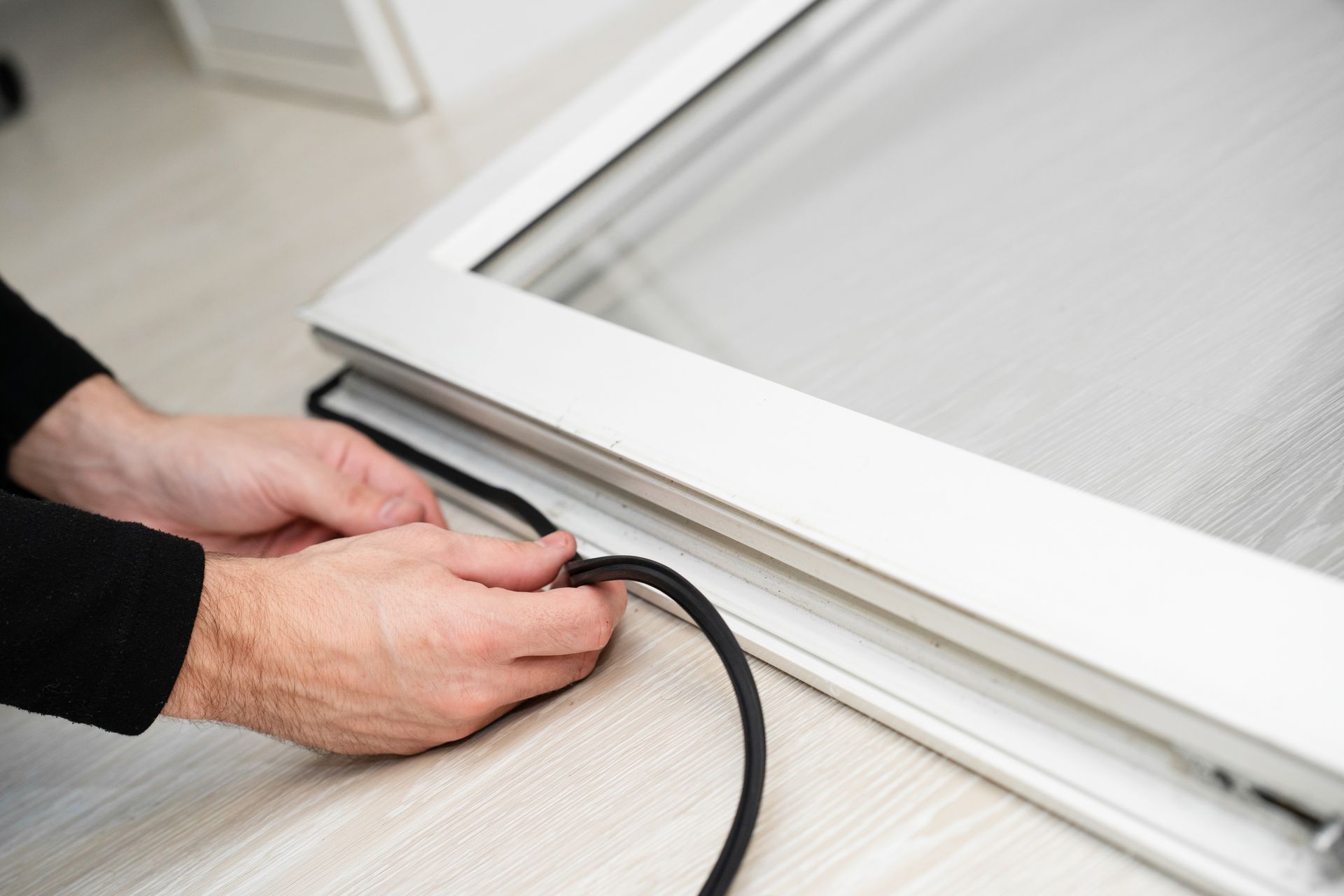 Hands securing a black cord around a white window frame or blind edge Hands securing a black cord around a white window frame or blind edge