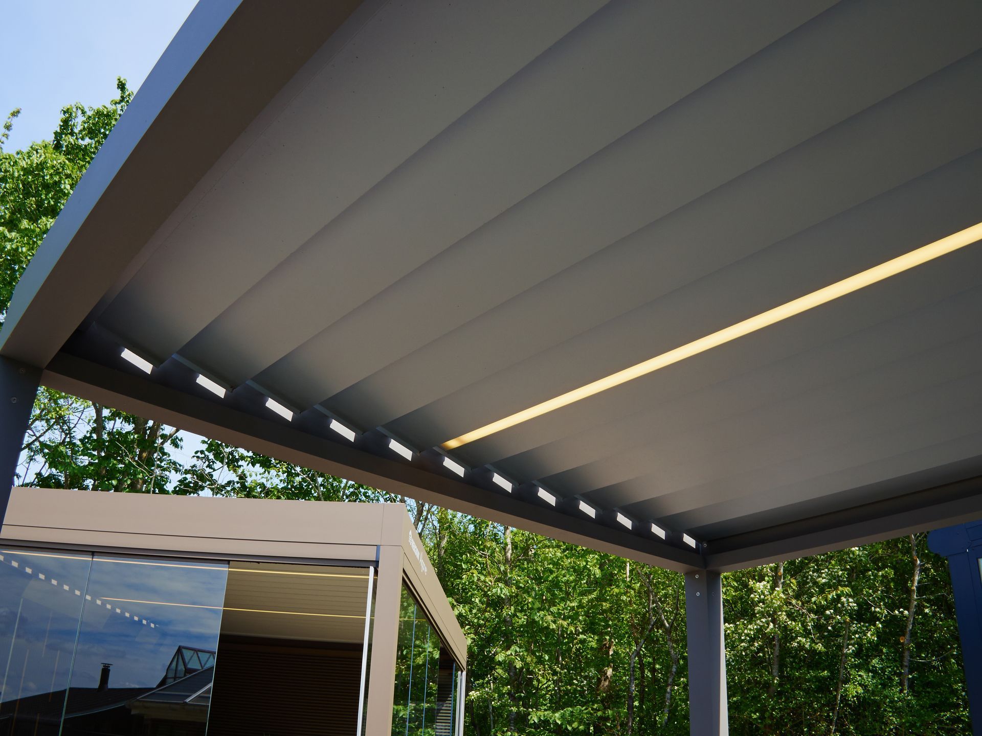 Modern patio with retractable roof, skylight strip, and trees in the background