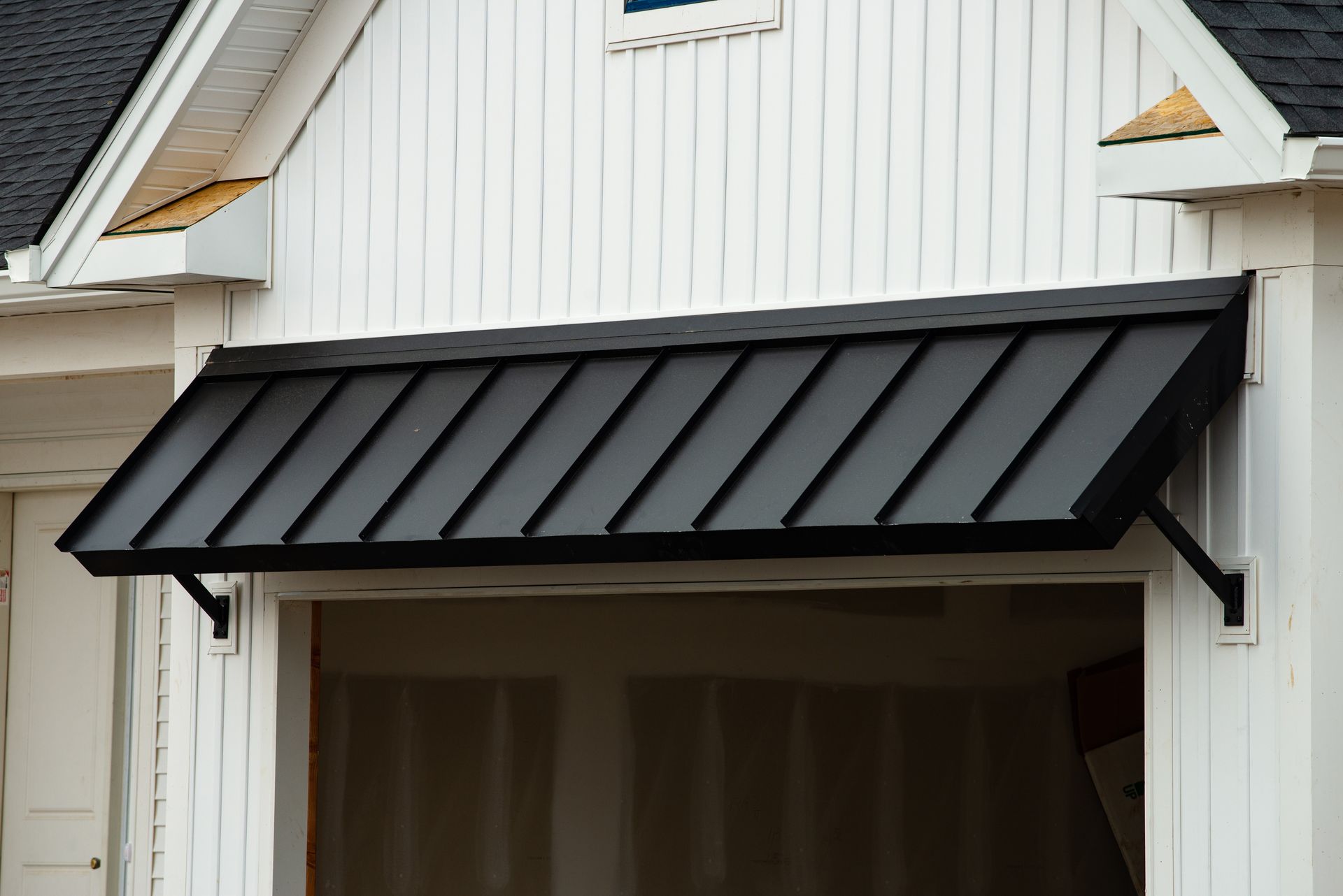 Black metal awning over a white garage door on a house exterior Black metal awning over a white garage door on a house exterior