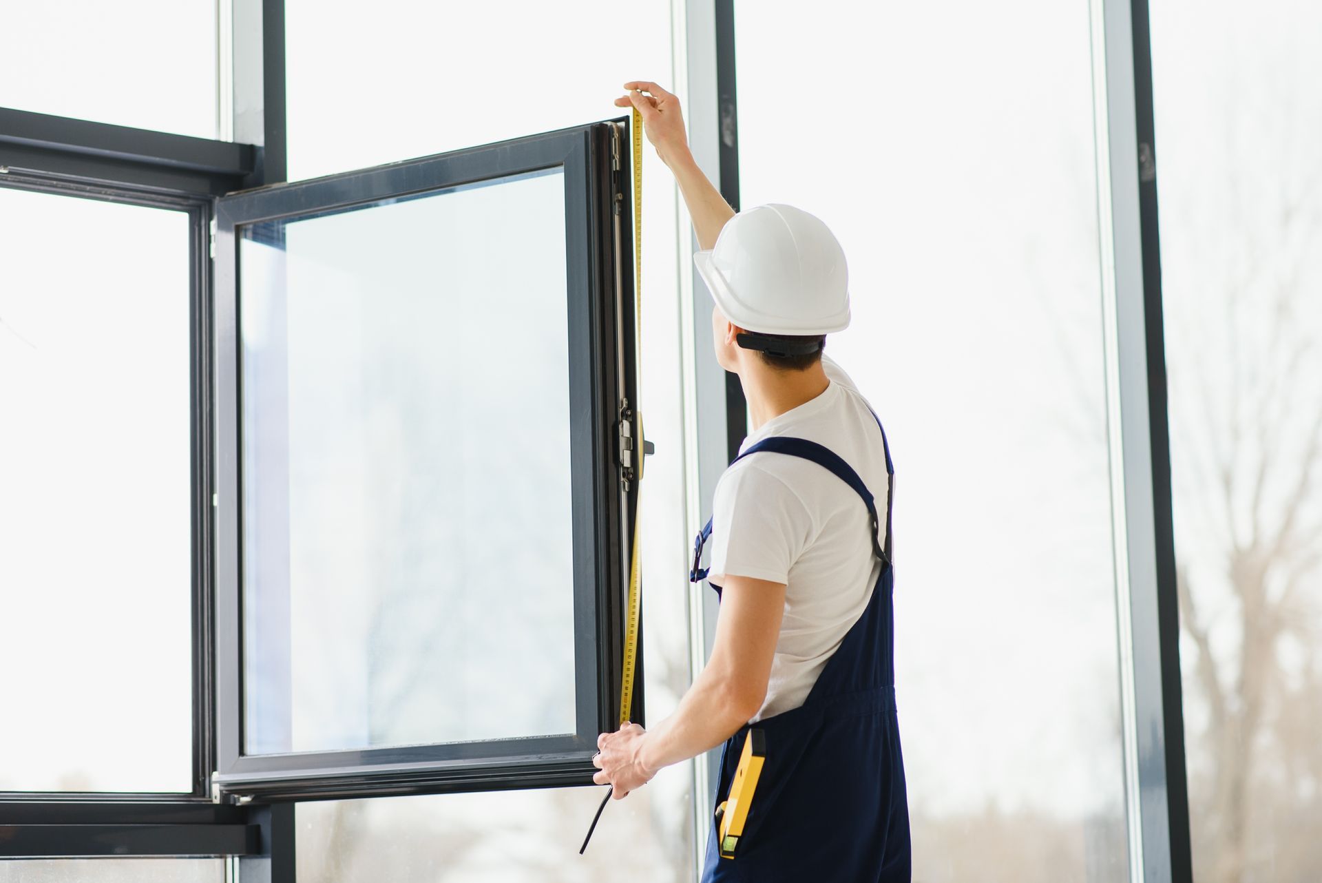 Person in a white hard hat opening a black-framed window indoors Person in a white hard hat opening a black-framed window indoors