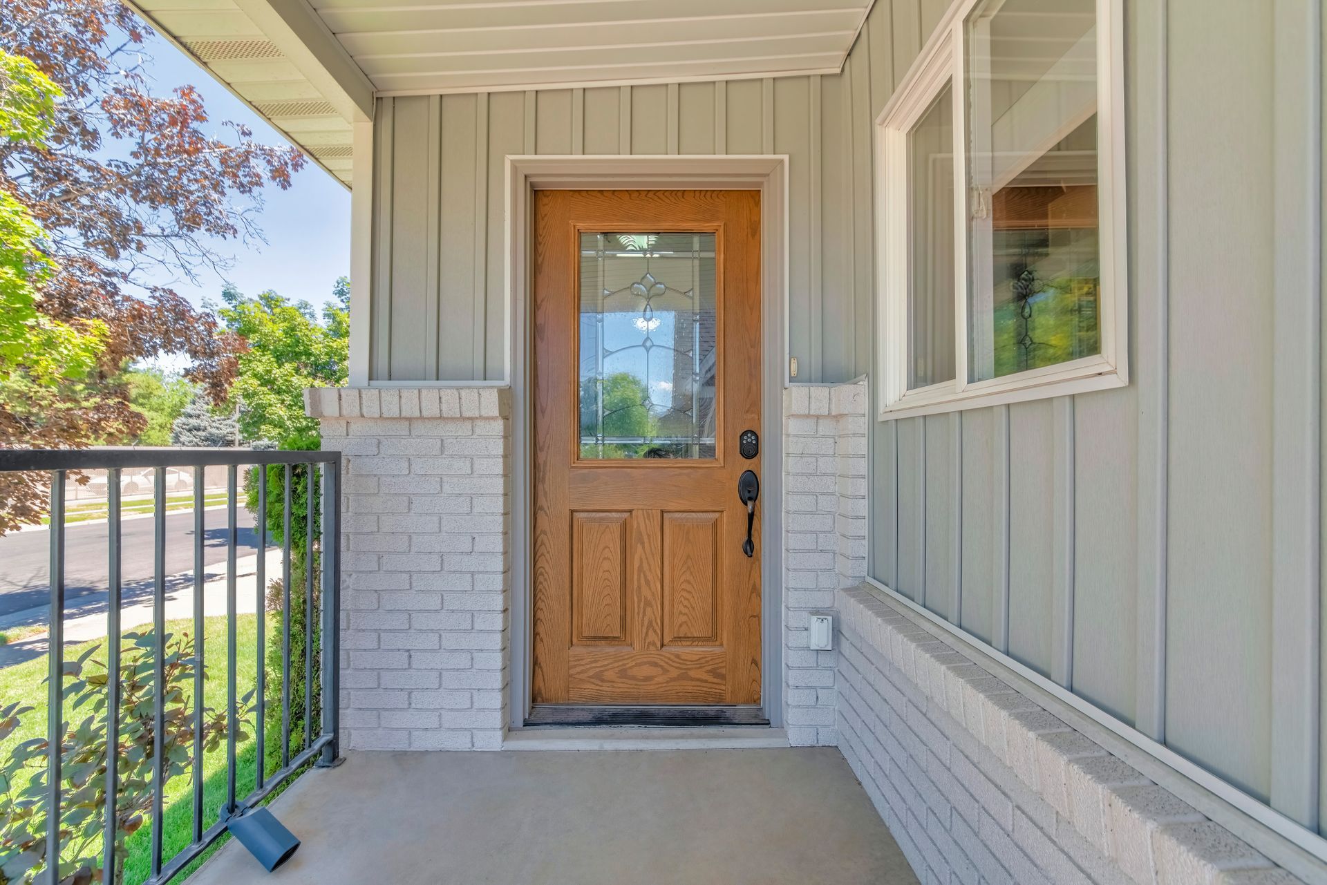 Covered porch with a wooden front door, white siding, and black railing overlooking a yard. Covered porch with a wooden front door, white siding, and black railing overlooking a yard.
