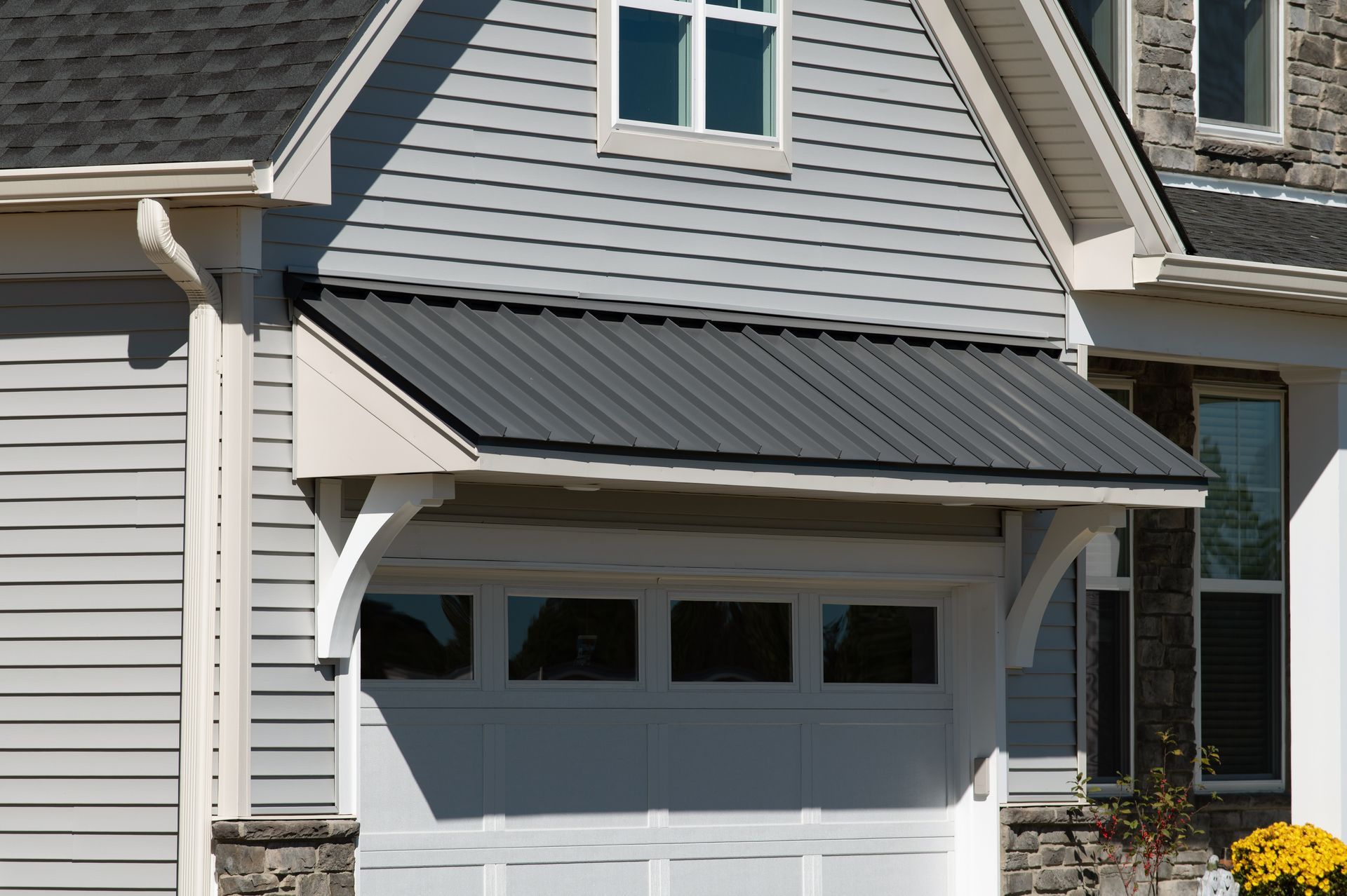 Suburban house exterior with white siding, dark awning, and a garage door Suburban house exterior with white siding, dark awning, and a garage door