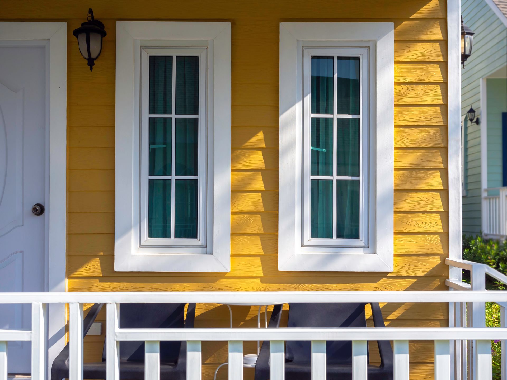 Yellow house porch with white-framed windows, lantern, and white railing in sunlight Yellow house porch with white-framed windows, lantern, and white railing in sunlight